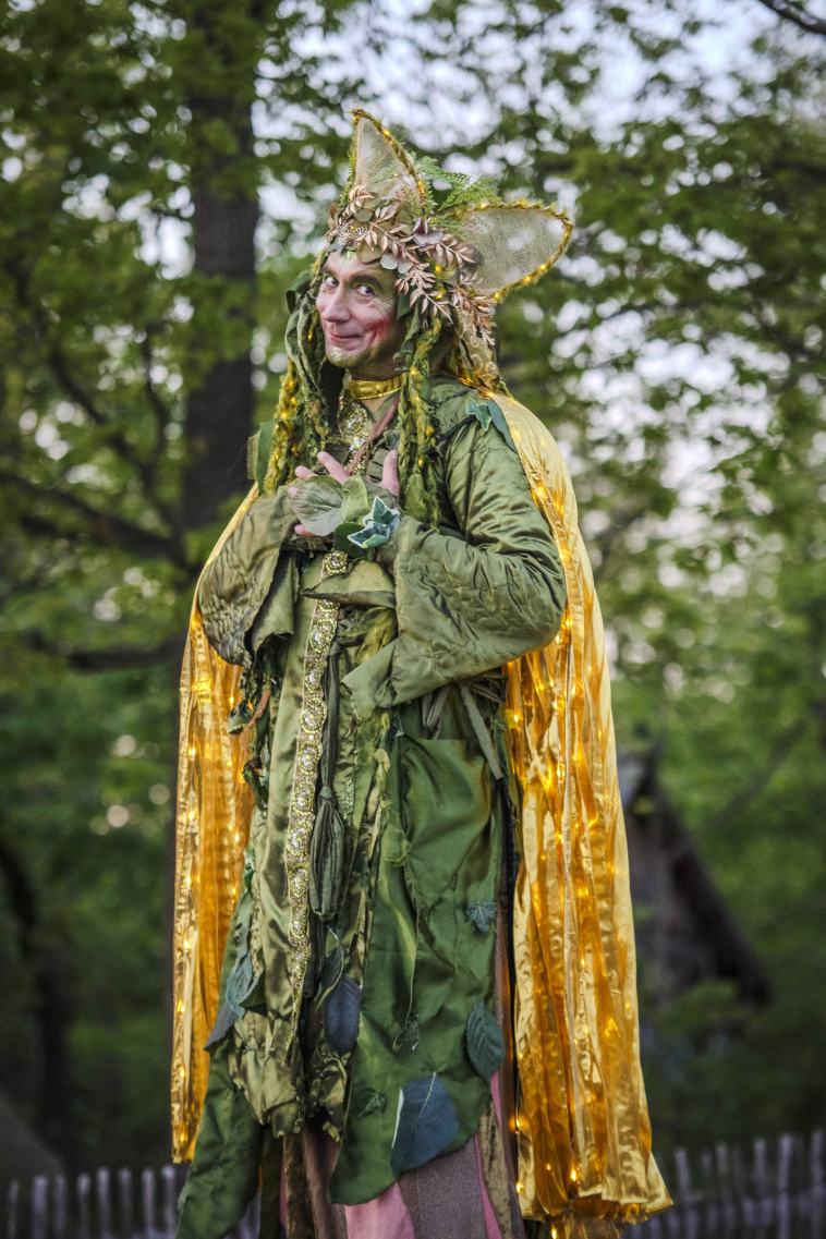 Stelzenfigur als Naturwesen in Grün und Gold mit Blätterkrone im Wald